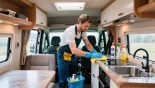Interieur van een camper waarin de keuken wordt schoongemaakt met schoonmaakmiddelen.