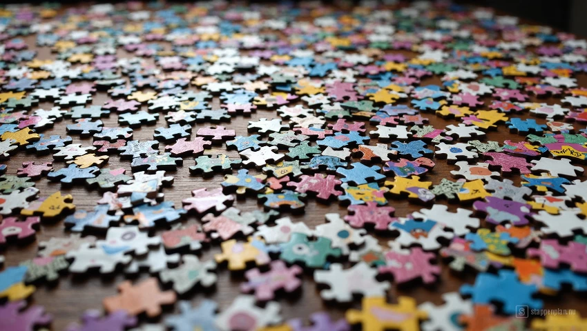 Tafel bedekt met duizenden puzzelstukjes, chaotische en kleurrijke scène.